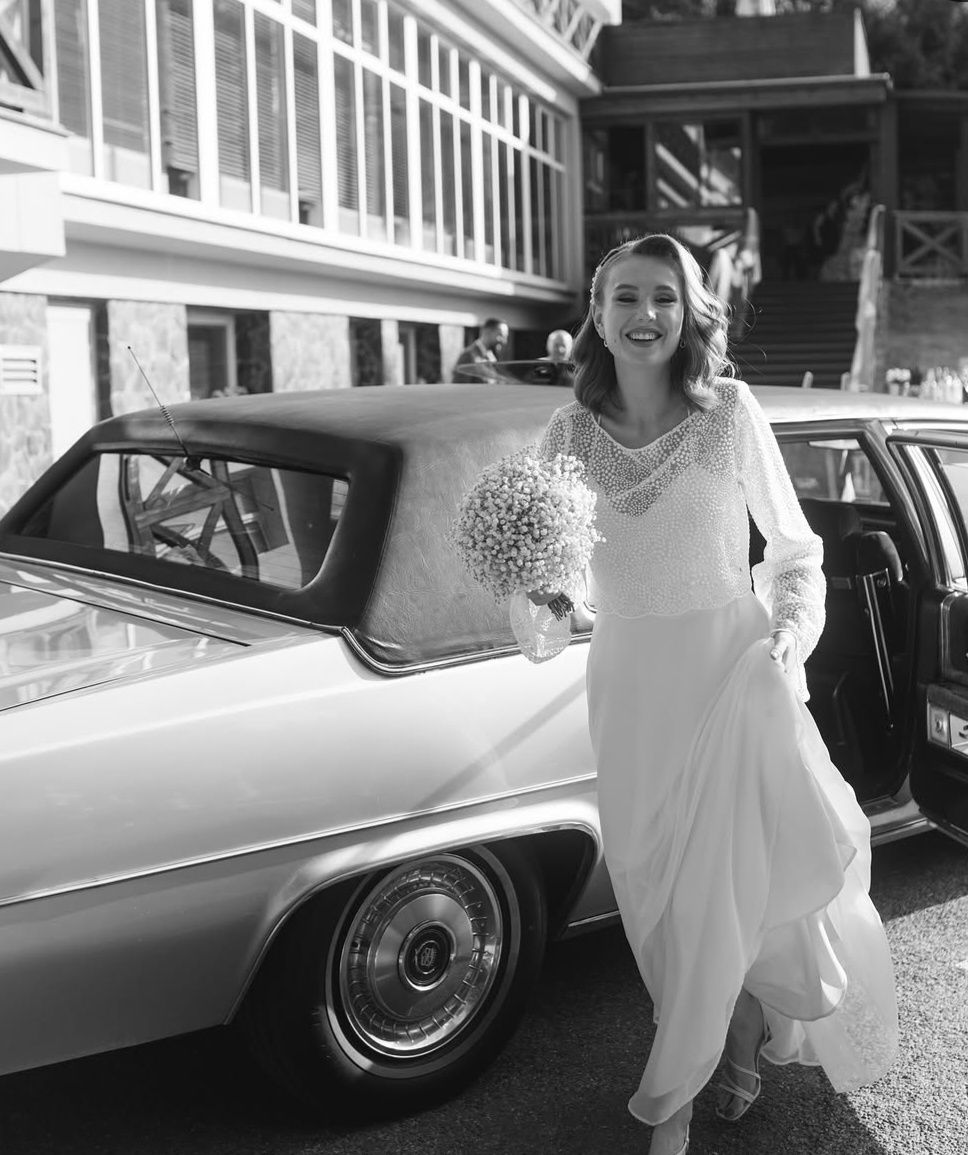 Usmiata nevesta s kyticou vystupujúca z Cadillacu, čiernobiela fotografia