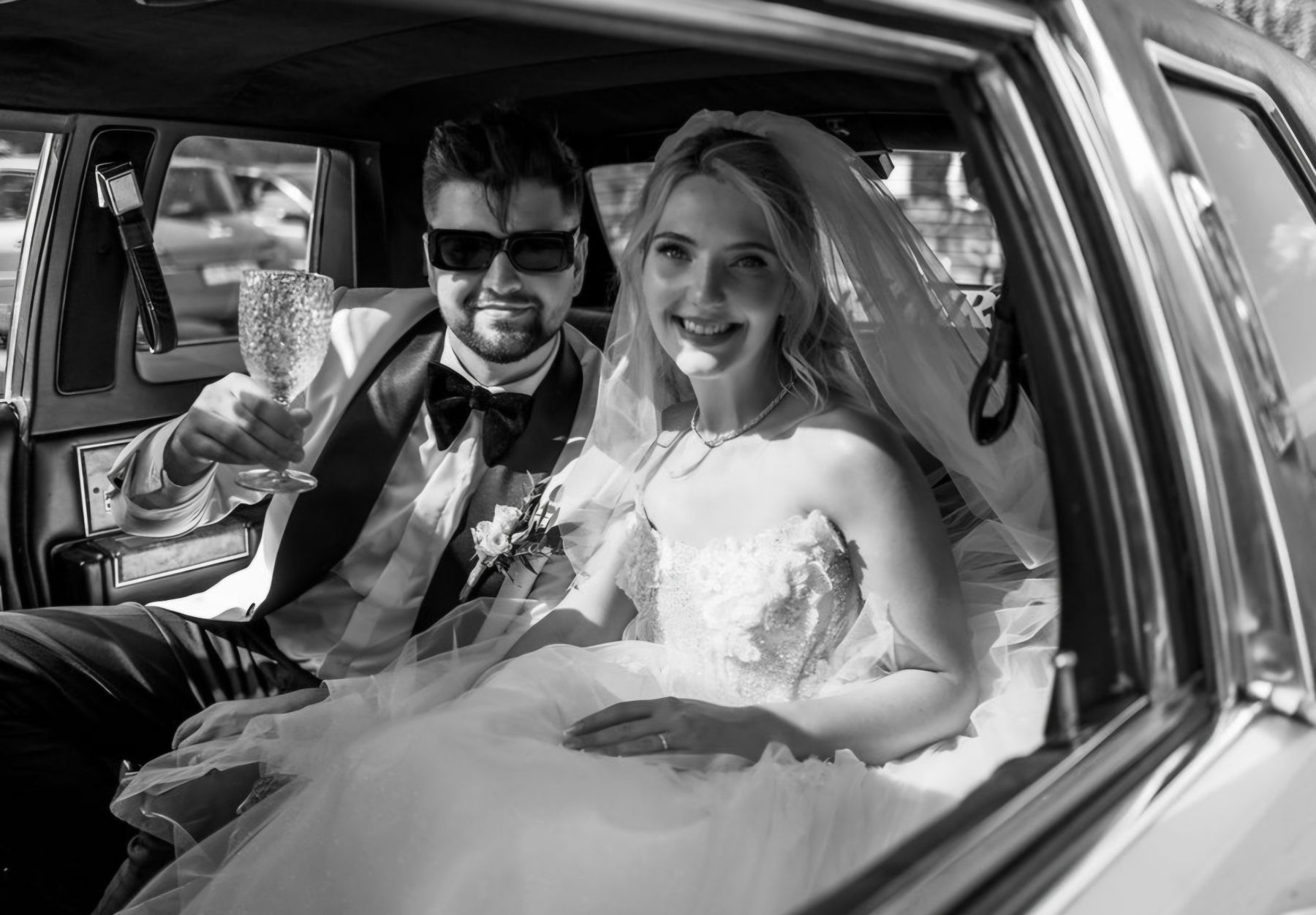 Novomanželia so šampanským vo vnútri Cadillacu, čiernobiela fotografia
